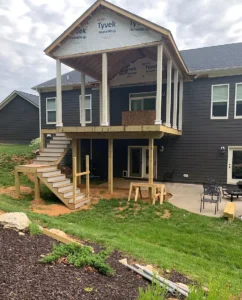 Back view of a dark gray house under construction, showing a large elevated deck with a covered porch roof