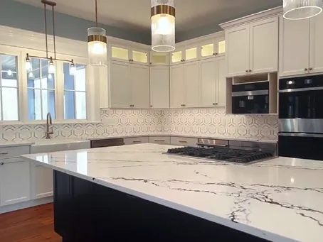 Modern kitchen featuring white cabinets, a marble countertop, black appliances, and elegant pendant lighting