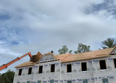Three-story apartment or townhouse building under construction, wrapped in house wrap, with a large orange dumpster in the foreground